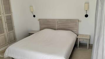 A bedroom with a bed, two nightstands, a wardrobe, and two wall-mounted lamps.