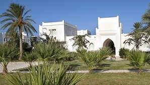 A white building with a central archway, surrounded by palm trees and a well-maintained lawn. - Parc Djerba Explore Residence (Aghir)