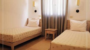 Habitació d'hotel amb dos llits individuals, una petita taula de nit de fusta i dues làmpades penjades a la paret.