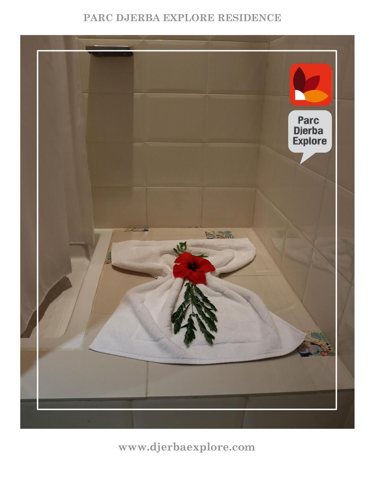Une salle de bain avec un espace douche, une serviette ornée d’une fleur rouge et l’adresse d’un site web.