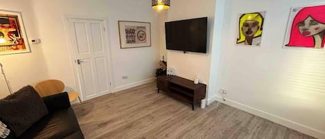 Un salón moderno con una televisión de pantalla plana, un sofá marrón oscuro, piso de madera y una lámpara colgante.