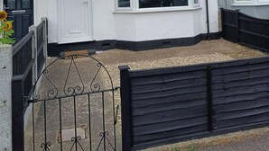 A two-story residential building with a white facade, a black front gate, and a small garden area. - Cool 2 Bed House Hornchurch, Arcade Games, Parking (Hornchurch)