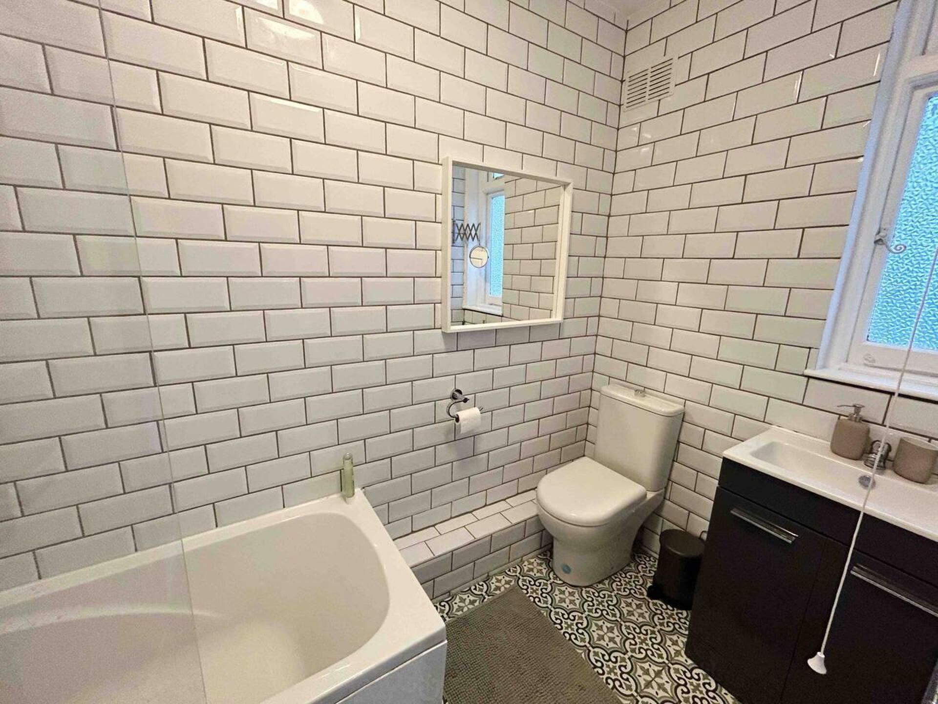 A bathroom with white subway tiles, a white toilet, a bathtub, and a sink with a mirror above it.