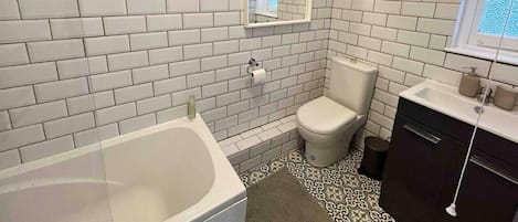A bathroom with white subway tiles, a white toilet, a bathtub, and a sink with a mirror above it.