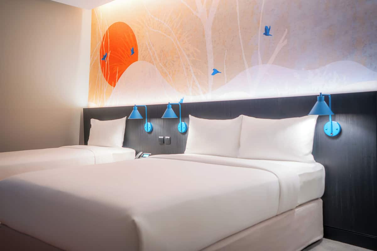 Una habitación de hotel con una cama grande, dos lámparas de noche y un mural en la pared.