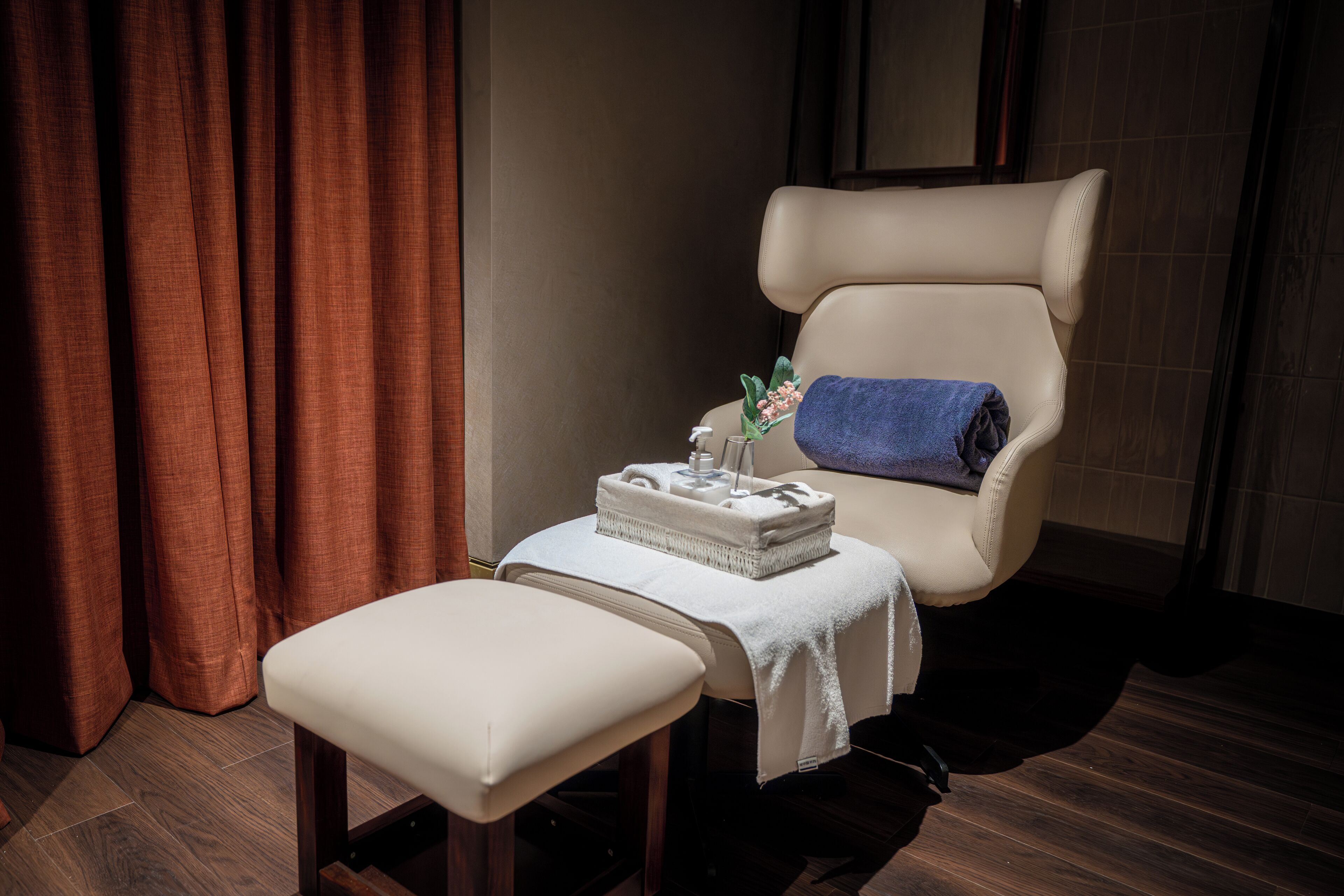 Una stanza spa con una poltrona massaggiante, un piccolo tavolo con un asciugamano e una bottiglia, e un pavimento in legno.