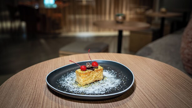 Un postre en un plato con azúcar glas sobre una mesa redonda en una habitación con poca luz y fondo desenfocado.