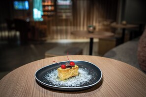 Un dolce su un piatto con zucchero a velo su un tavolo rotondo in una stanza scarsamente illuminata, con sfondo sfocato.
