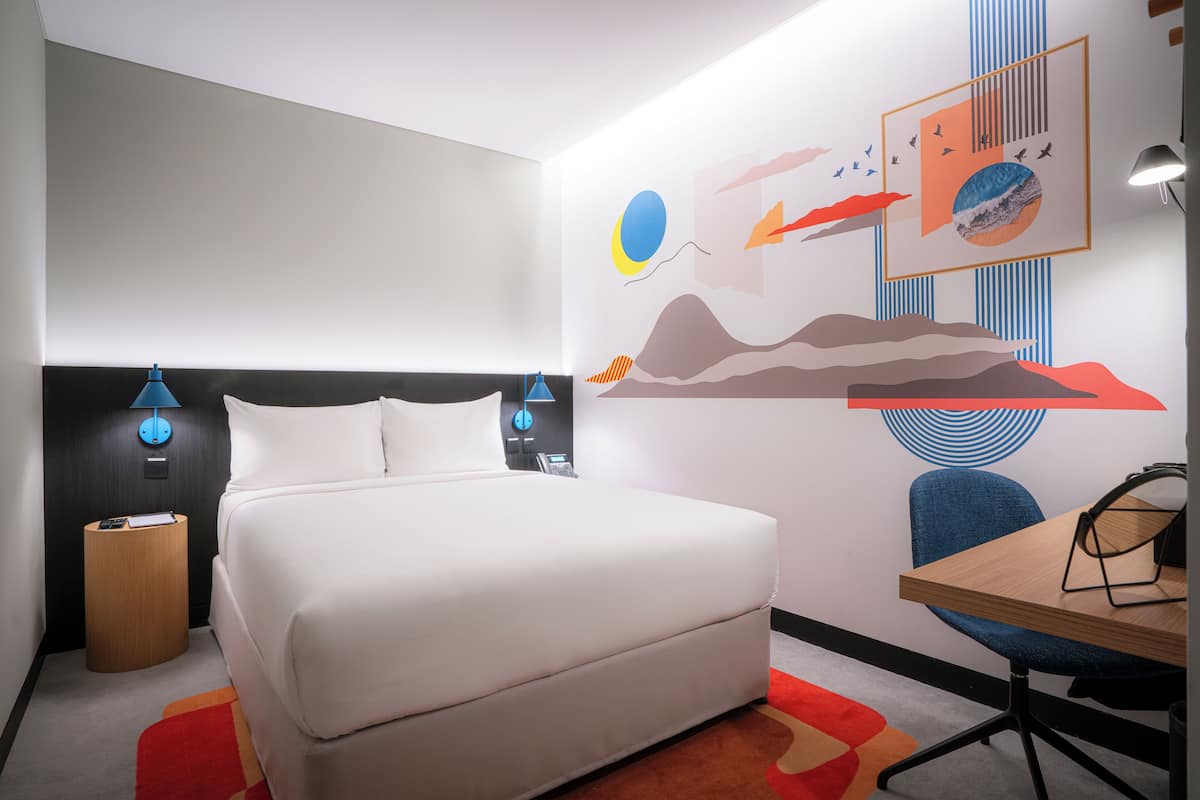 Una habitación de hotel moderna con una cama grande, un escritorio y un mural en la pared.