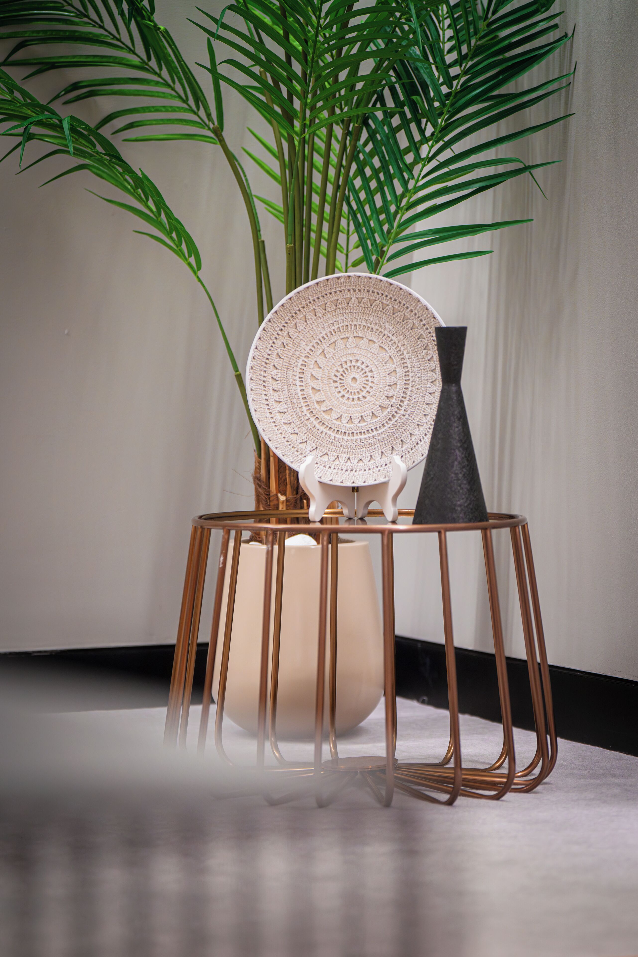A chair with a crocheted backrest, a vase, and a tall plant in a corner.