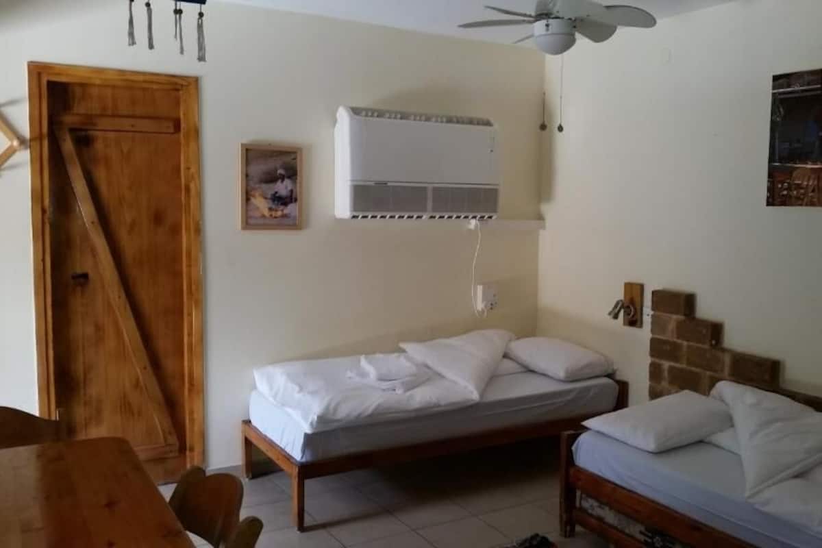Ein Zimmer mit zwei Betten, einer Holztür, einer Klimaanlage und einem Bild an der Wand.
