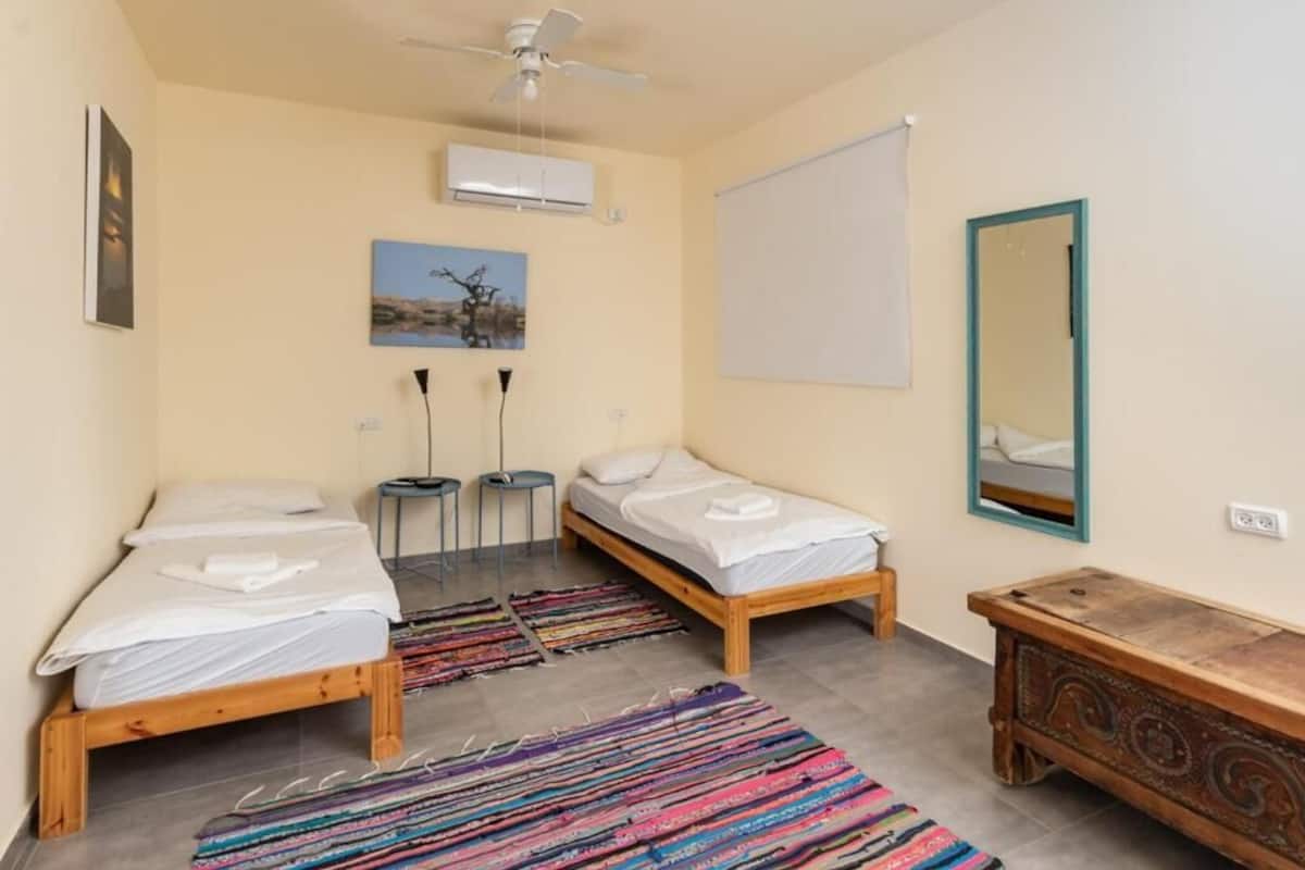 Ein Schlafzimmer mit zwei Einzelbetten, einem Deckenventilator, einer Klimaanlage, einem Spiegel und einer Holzkommode.