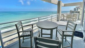 Ein Balkon mit Tisch und Stühlen mit Blick auf einen Strand und den Ozean.