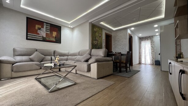 Un salon moderne avec un canapé d’angle, une table basse en verre et un coin repas comprenant une table et des chaises en bois.