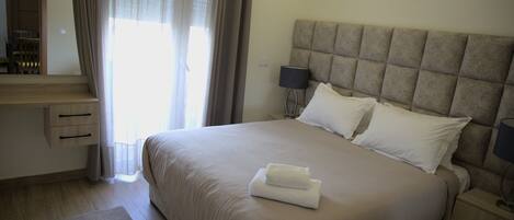 A neatly made bed with a headboard, a bedside table with a lamp, and a window with curtains.