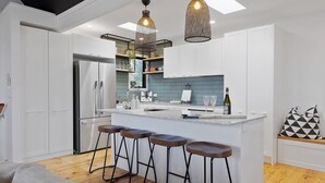 Una cocina moderna con armarios blancos, una isla central con taburetes, iluminación colgante y un salpicadero.