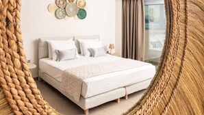 A bedroom with a large woven mirror, a bed with white bedding, a nightstand, and a wall art piece.