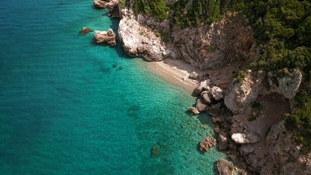 A coastal landscape with clear turquoise waters, rocky cliffs, and dense green vegetation.