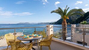 A terrace with yellow wicker chairs and a table set for two, overlooking a body of water and a mountainous landscape.