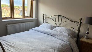 A neatly made bed with a metal frame, a window with a view of buildings, and a bedside table with a lamp. - Beautiful City Centre Apartment-cathedral Views (Norwich)