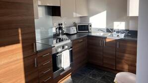 A modern kitchen with wooden cabinets, stainless steel appliances, and a black countertop. - Beautiful City Centre Apartment-cathedral Views (Norwich)