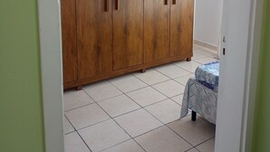Huoneessa on suuri puinen vaatekaappi, laatoitettu lattia ja kuvioitu päiväpeitteellä varustettu sänky.