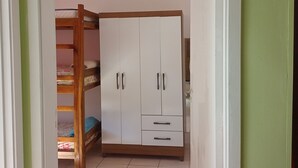 Huoneessa on kerrossänky, valkoinen vaatekaappi, jossa on kaksi laatikkoa, ja laattalattia.