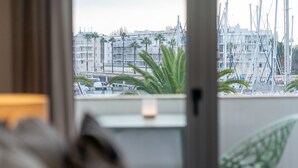 A view through a window with a balcony, featuring a cityscape with buildings and palm trees. - Captain's Quarters at Lagos Marina (Lagos)
