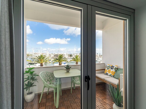 A balcony with a view of a marina, a table, chairs, and potted plants.