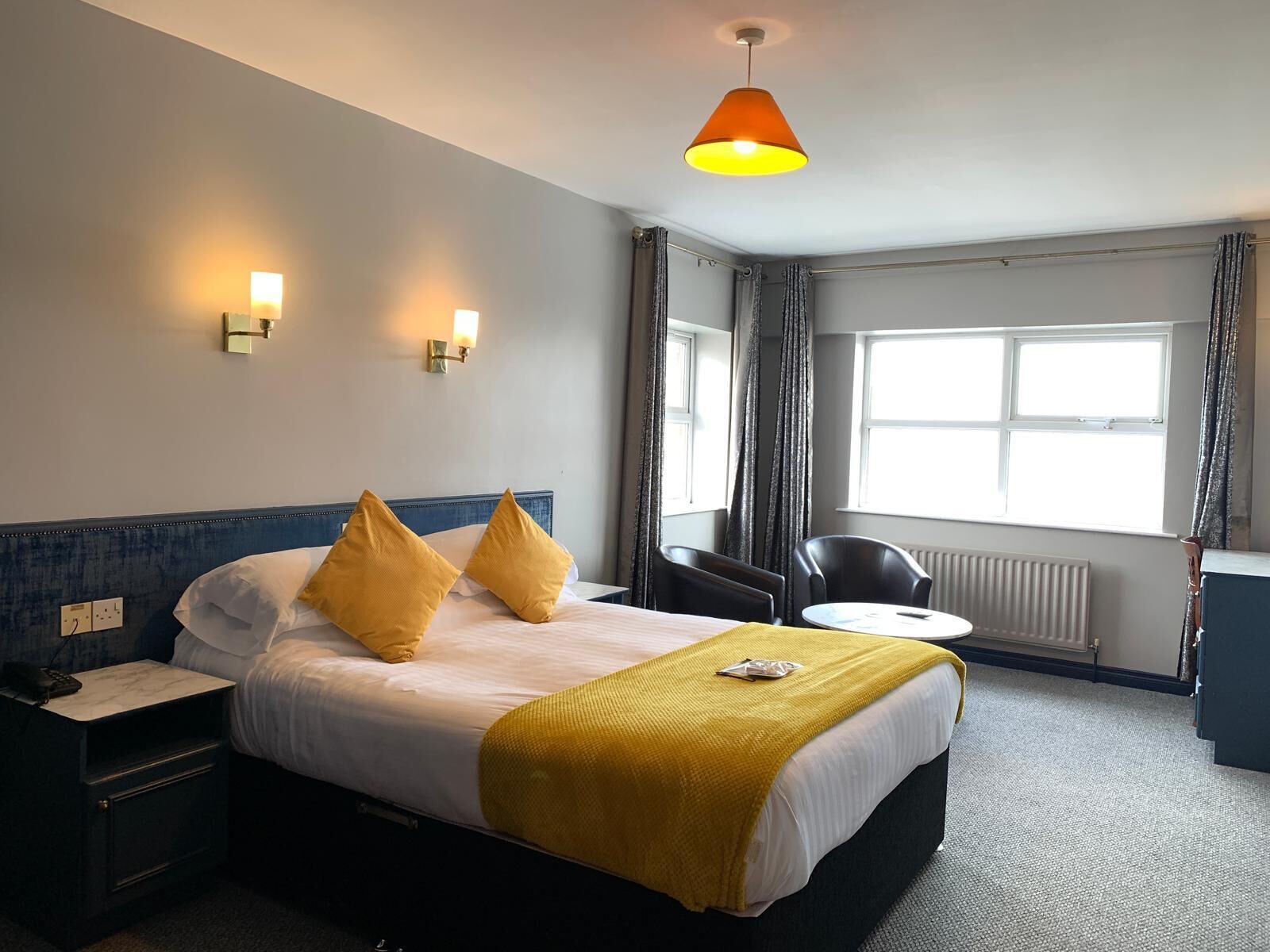 A hotel room with a bed, bedside table, lamp, chair, and a window with curtains.