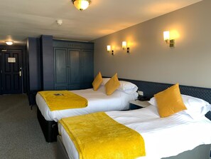 A hotel room with two beds, each with white linens and yellow throw blankets. There are wall-mounted lights and a dark-colored wardrobe. - The Donard (Newcastle)