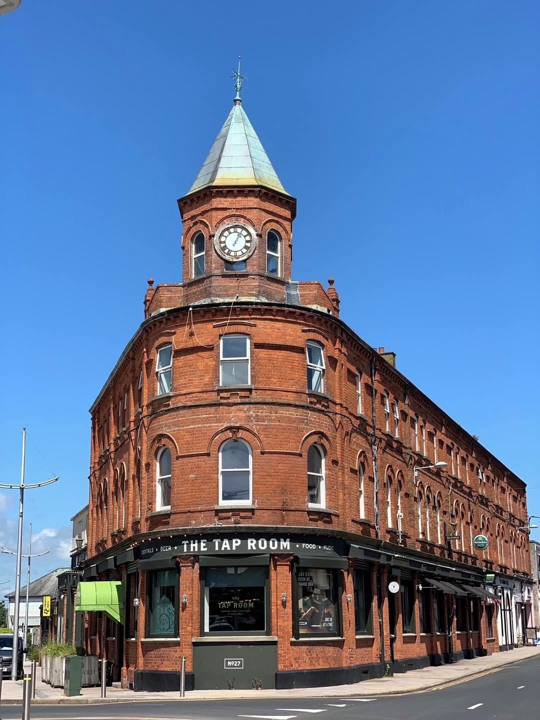 A historic red brick building with a clock tower and a sign for 'The Tap Room' on the ground floor.