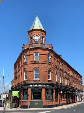 A historic red brick building with a clock tower and a sign for 'The Tap Room' on the ground floor. - The Donard (Newcastle)