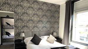 A hotel room with a large bed, a bedside table with a lamp, a wardrobe, and a window with curtains. - The Donard (Newcastle)