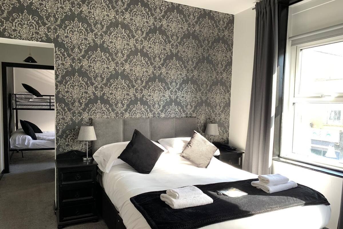 A hotel room with a large bed, a bedside table with a lamp, a wardrobe, and a window with curtains.