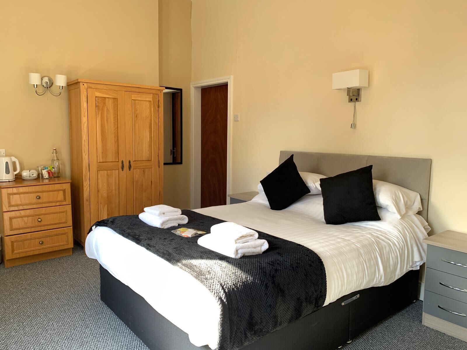 A hotel room with a bed, a wardrobe, a nightstand, and a wall-mounted lamp.