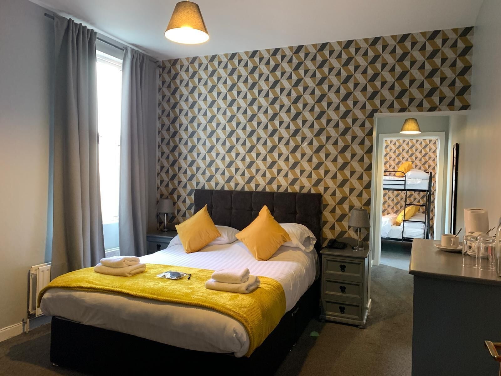 Una habitación de hotel con una cama, mesitas de noche, un espejo y un aparador.