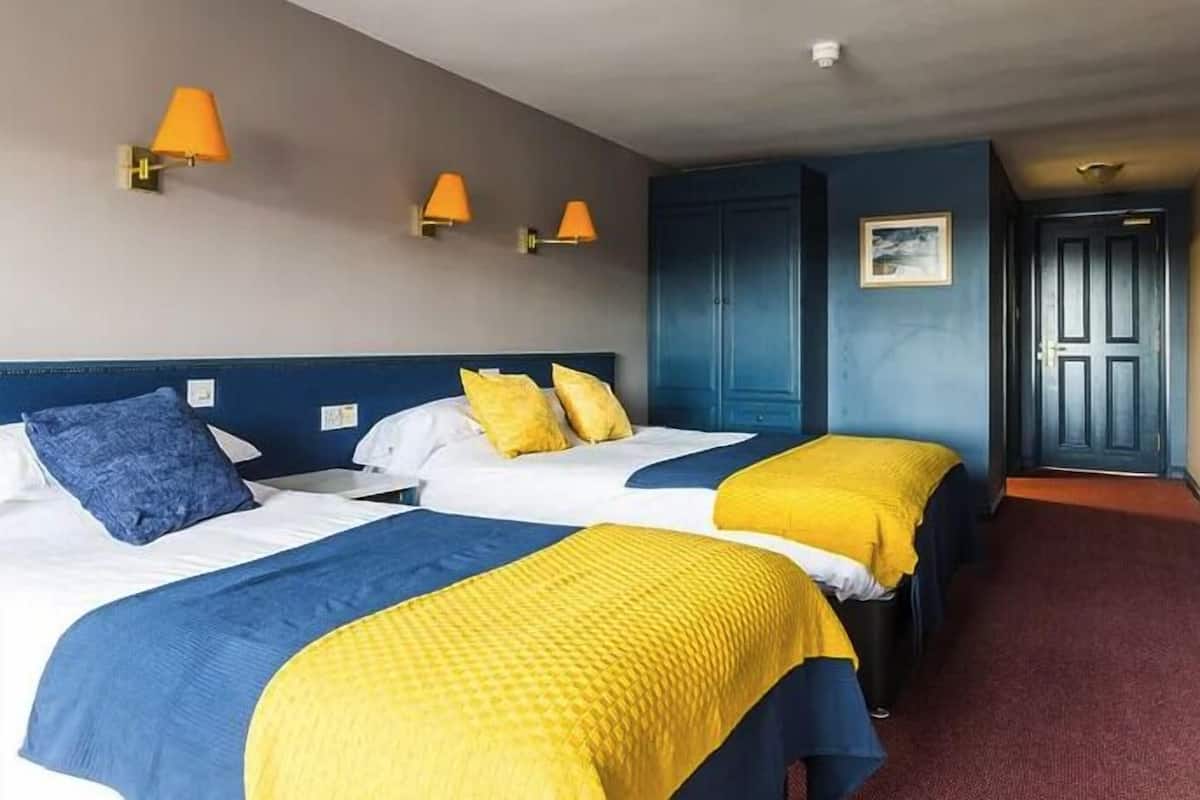 A hotel room with two beds, each with a blue and yellow bedspread, and a blue wardrobe.
