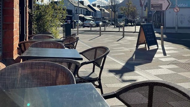 Outdoor seating with tables and chairs, a clear sky, and a street with buildings and signs. - The Donard (Newcastle)