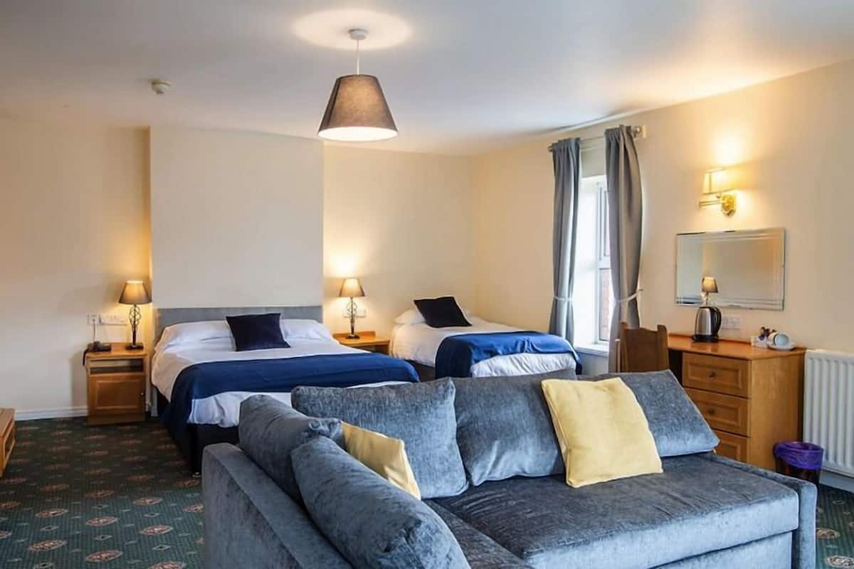A hotel room with two beds, a sofa, a desk, and a window with curtains.