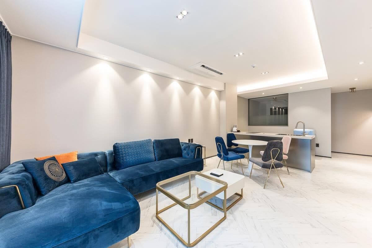 Un salon moderne avec un canapé bleu, une table basse en verre et un coin repas comprenant des chaises et une petite table.