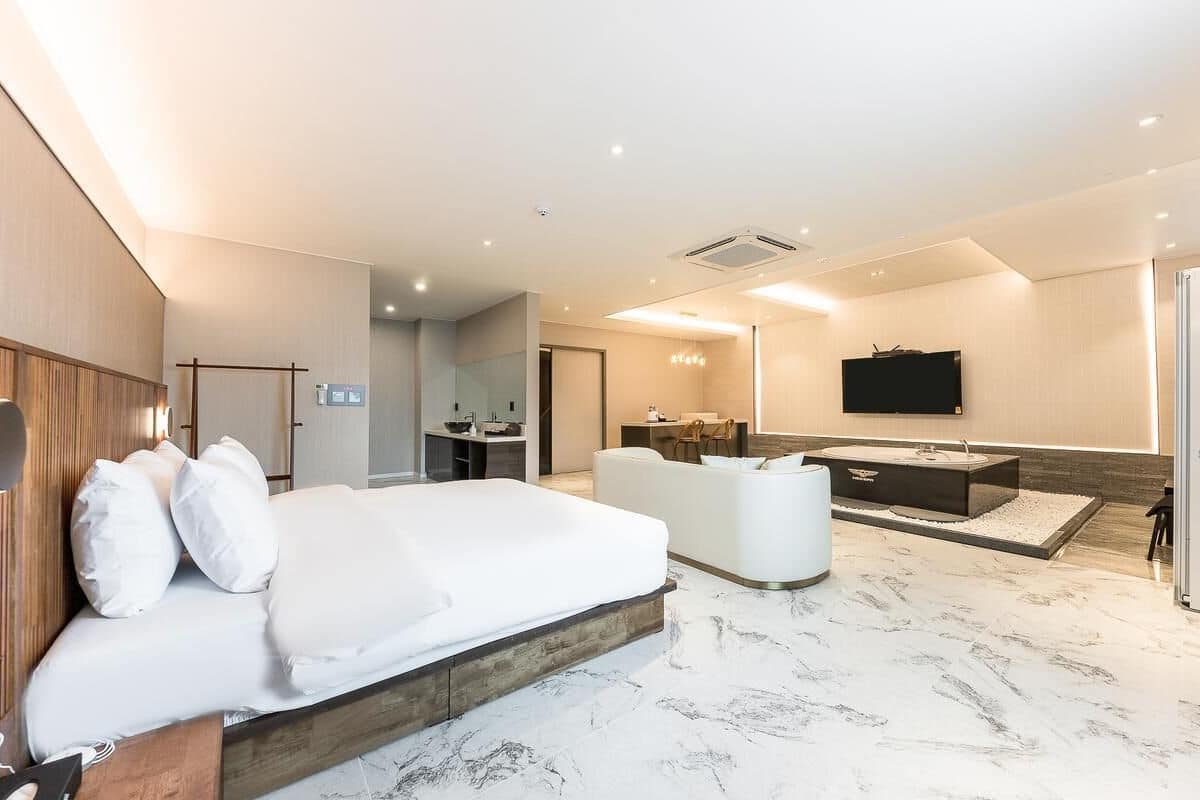 Une chambre d’hôtel moderne dotée d’un grand lit, d’un coin salon, d’une salle de bain avec un meuble-lavabo et un miroir, et d’une télévision.