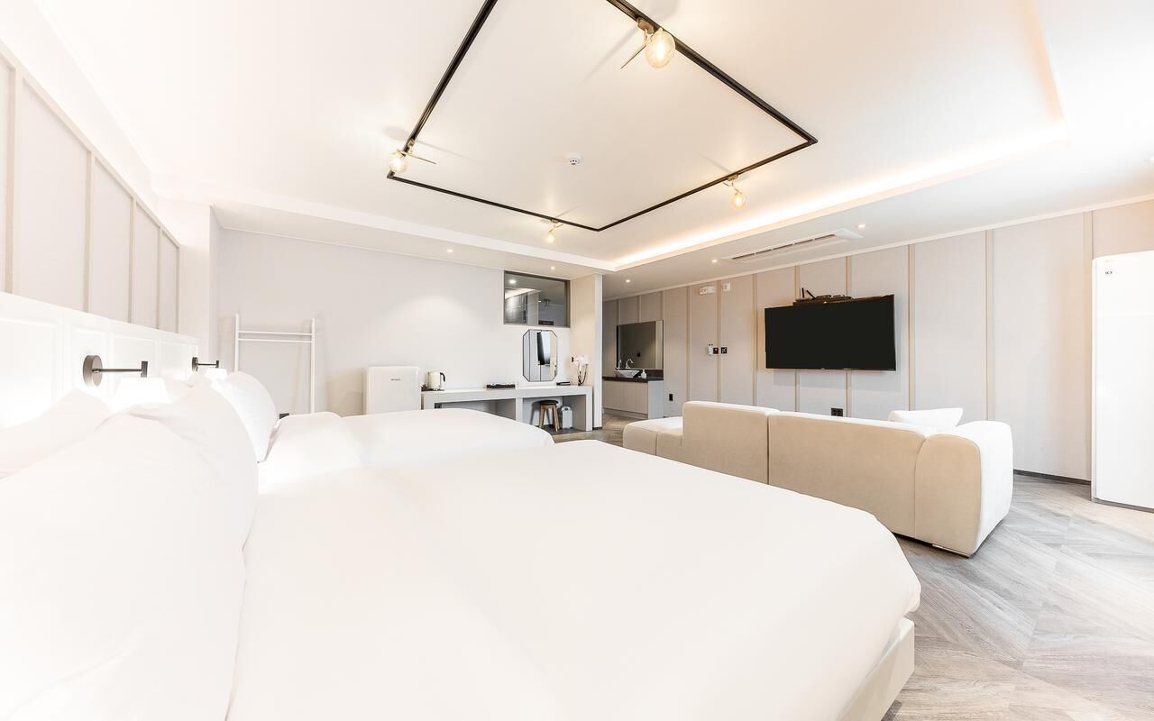 Una habitación de hotel moderna con una cama grande, un sofá, un televisor y una kitchenette.