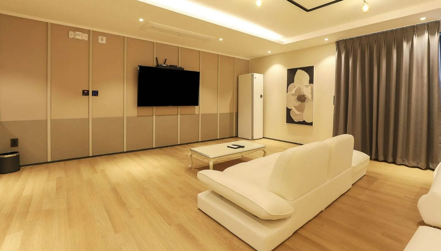 Una sala de estar moderna con un sofá, un televisor de pantalla plana, una mesa de centro y un ventanal con cortinas.