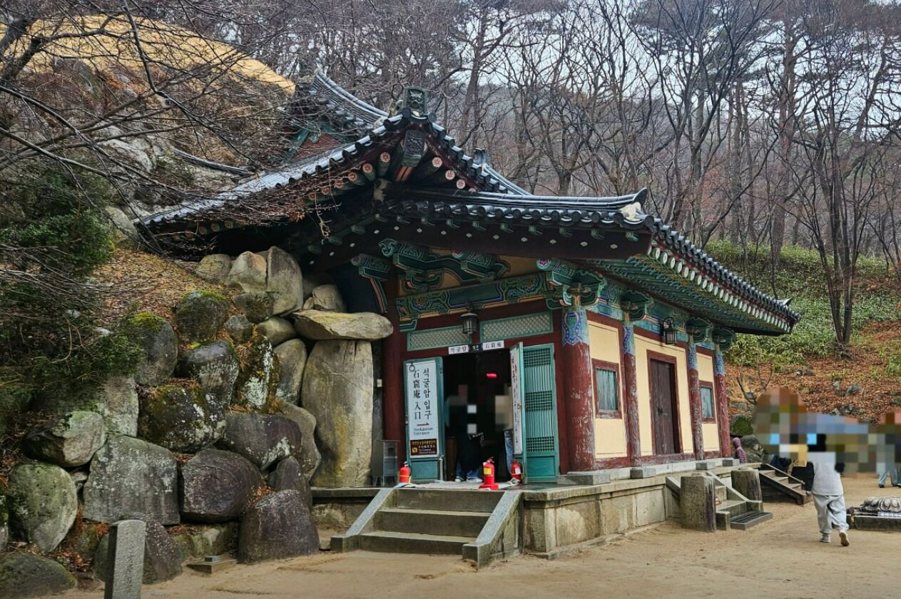 A traditional Korean temple with a tiled roof, stone walls, and a stone pathway leading to the entrance.