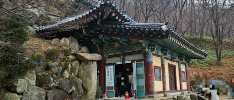 A traditional Korean temple with a tiled roof, stone walls, and a stone pathway leading to the entrance.