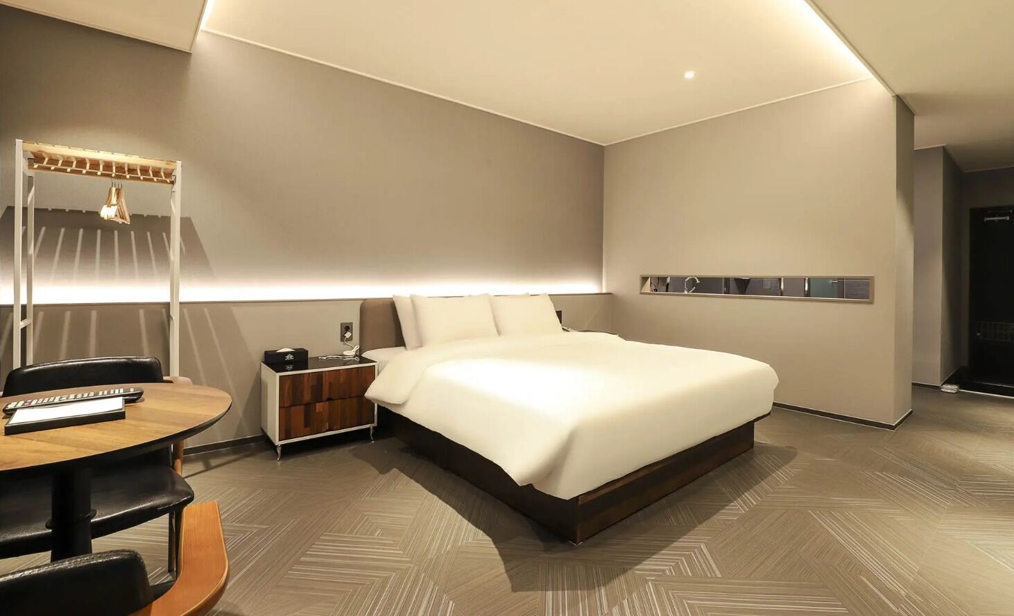 A modern hotel room with a large bed, a desk with a chair, a lamp, and a small cabinet.