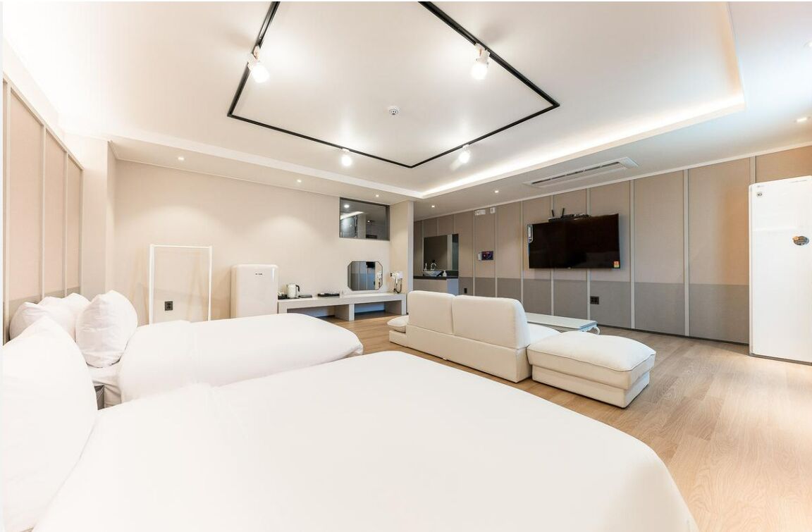 A modern hotel room with a large bed, a seating area with a TV, and a kitchenette.