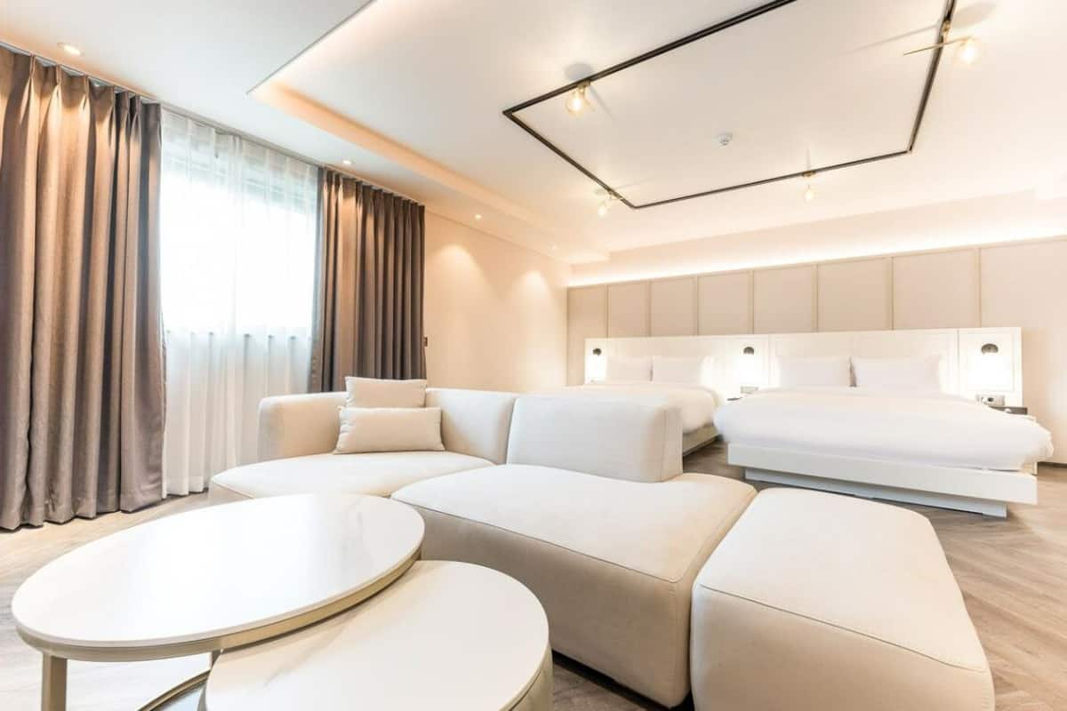 Une chambre d’hôtel moderne avec un canapé d’angle, un lit et une table basse ronde.
