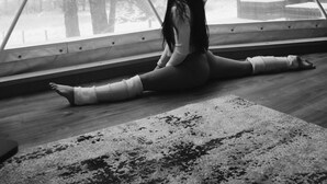 Une personne effectue une posture de yoga dans une pièce dotée d’une grande fenêtre, d’un plancher en bois et d’un tapis.